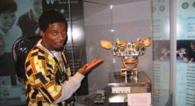 Ebah Patrick Ngole posing with a display case in an African-pattern shirt.